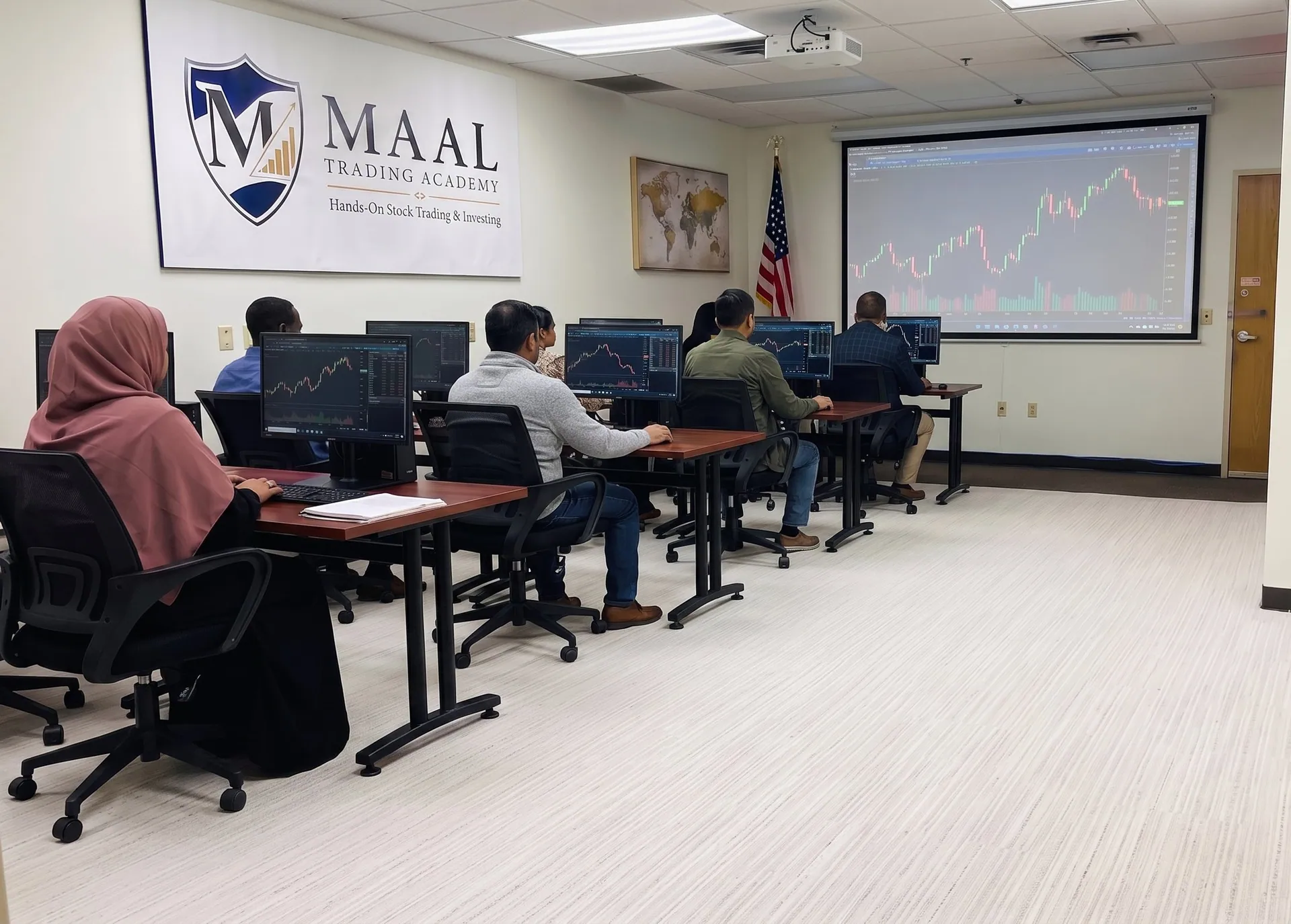 A beginner class in the MAAL TRADING ACADEMY room, charts on the projector.